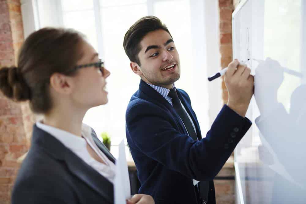 Professional financier analyzing his ideas on whiteboard and explaining them to colleague